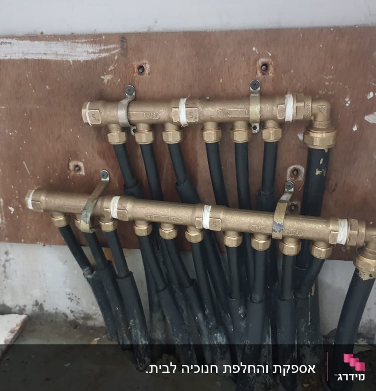 צינורות שחורים מחוברים למפצל פליז על קיר עץ